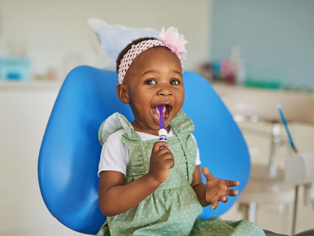 picture of child in dental chair putting toothbrush in mouth